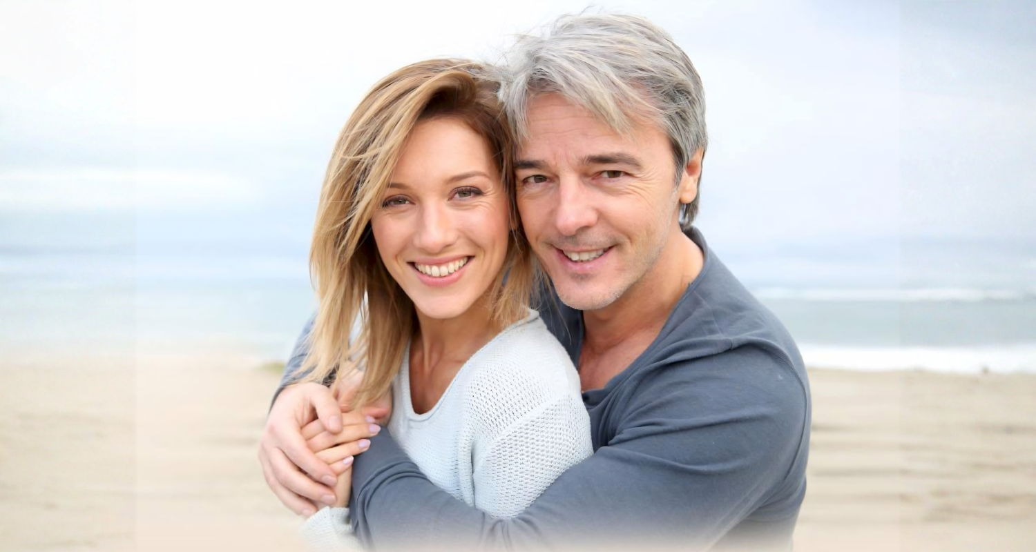 A smiling mature couple embracing on a beach — finding joy and companionship again